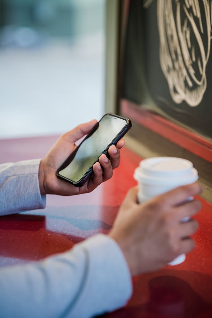 Close-up of a Man Holding a Disposable Coffee Cup and Using Phone